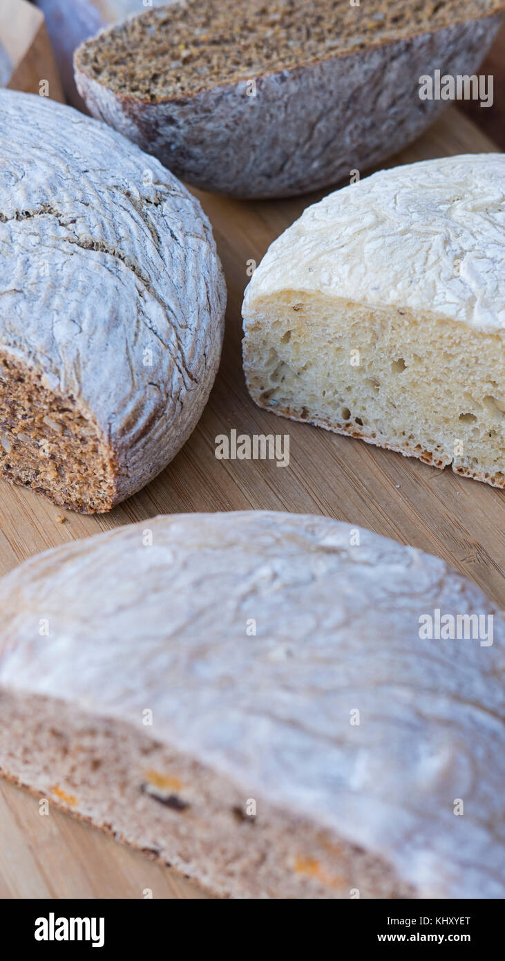 Colpo verticale di diversi tipi di sano, pane organico: marrone, bianco, con noci e semi, tagliati a metà e visualizzati su un pannello di legno Foto Stock