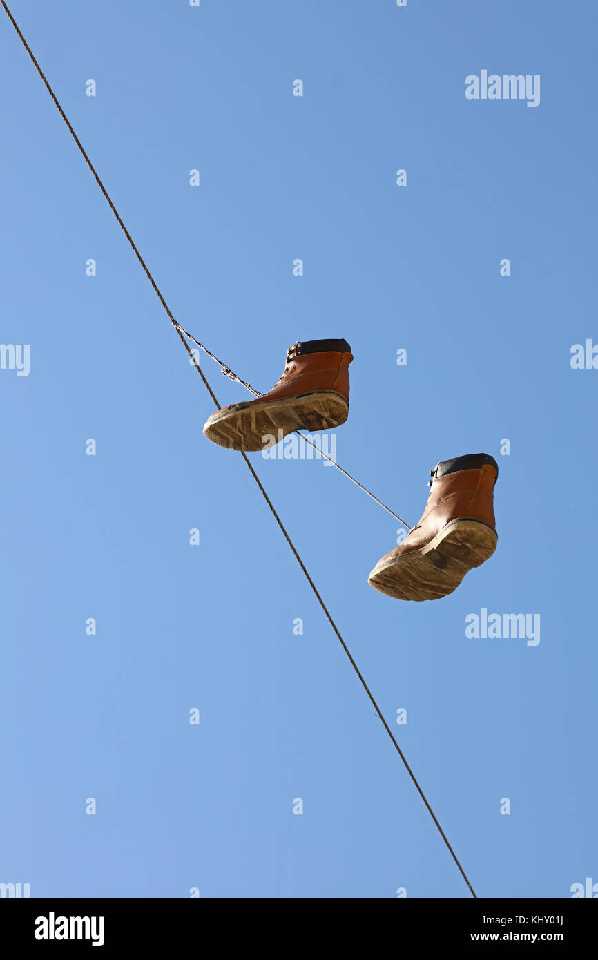 Coppia di vecchi indossato stivali marrone appeso su una linea telefonica filo come urbana tradizionale scherzo della gioventù, oltre il cielo azzurro, a basso angolo di visione Foto Stock