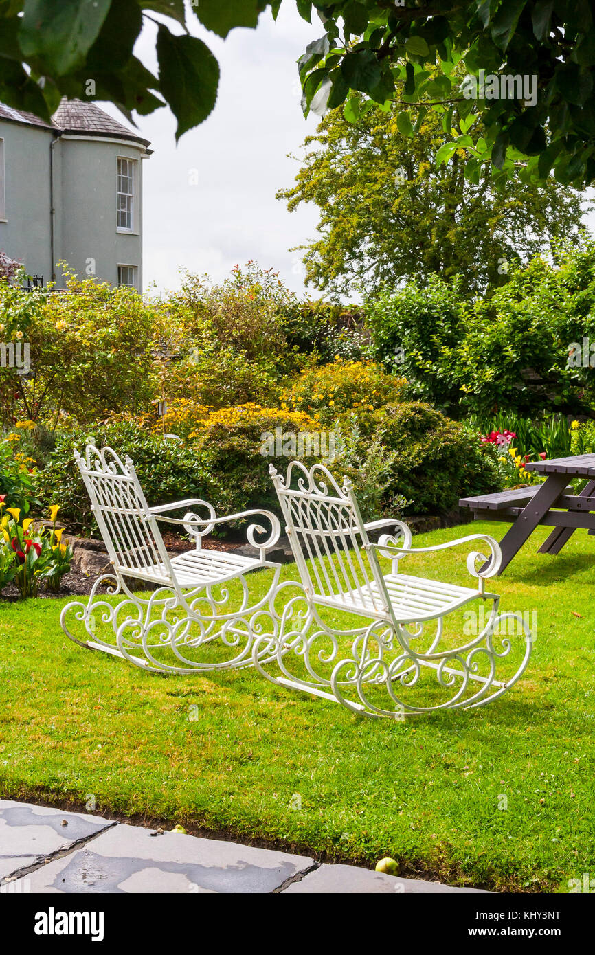 Coppia di vecchio stile vintage white ferro battuto sedie a dondolo in un  lussureggiante giardino con alberi e cespugli Foto stock - Alamy