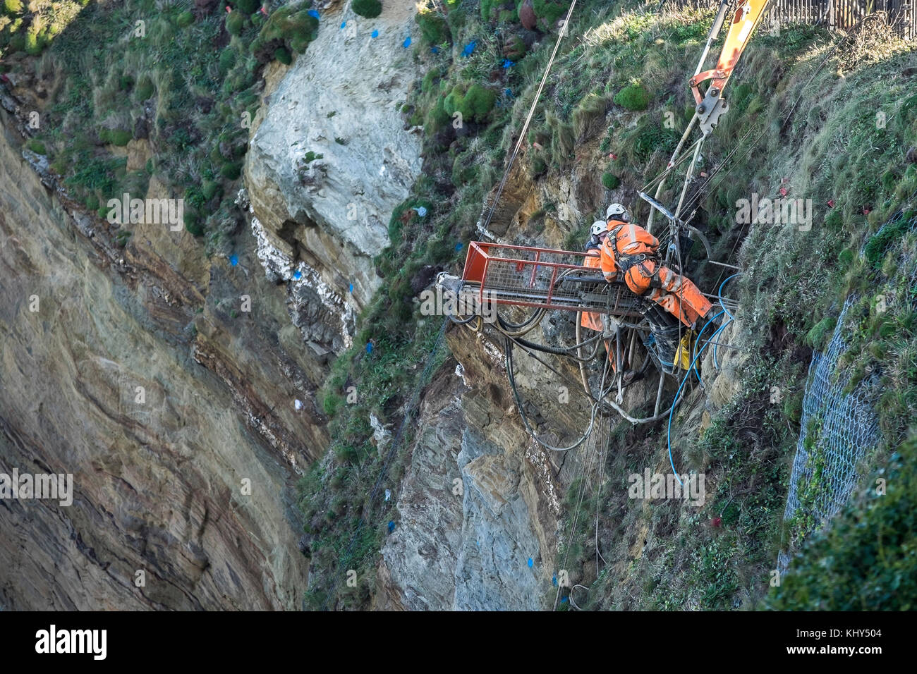 Due lavoratori di trapanare i fori nel rendere instabile la rupe sopra Tolcarne Beach in Newquay Cornwall Regno Unito. Foto Stock