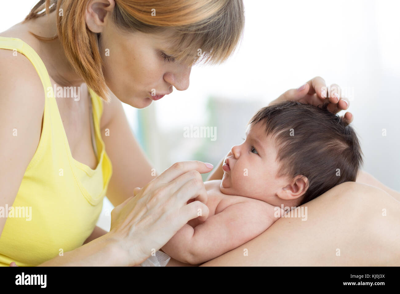 Vista laterale di madre premurosa e del suo neonato bambino guardando ogni altro, di trascorrere del tempo insieme a casa Foto Stock