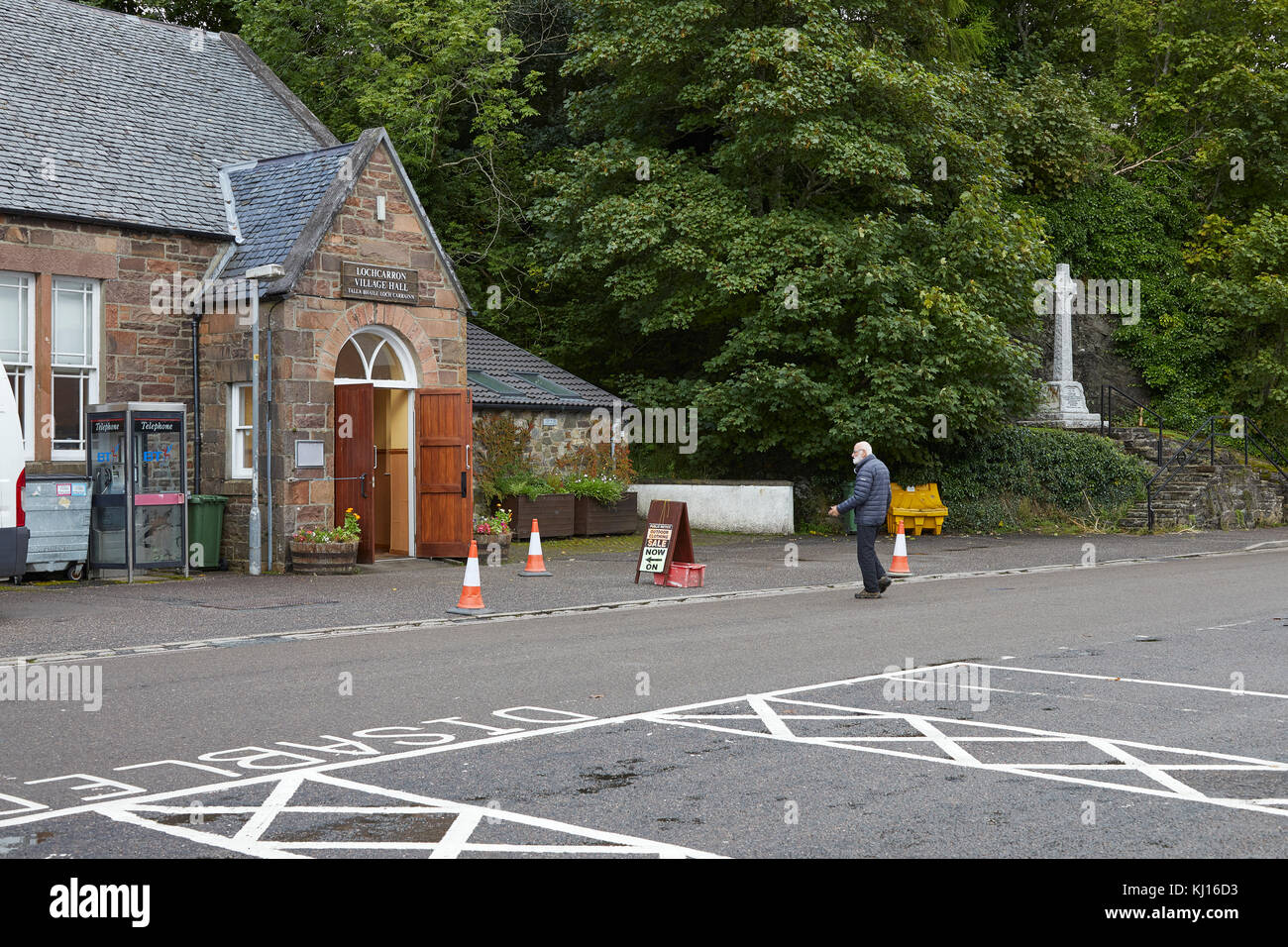 Un gentiluomo che si dirige verso il Lochcarron Village Hall e un negozio di abbigliamento all'aperto. Foto Stock