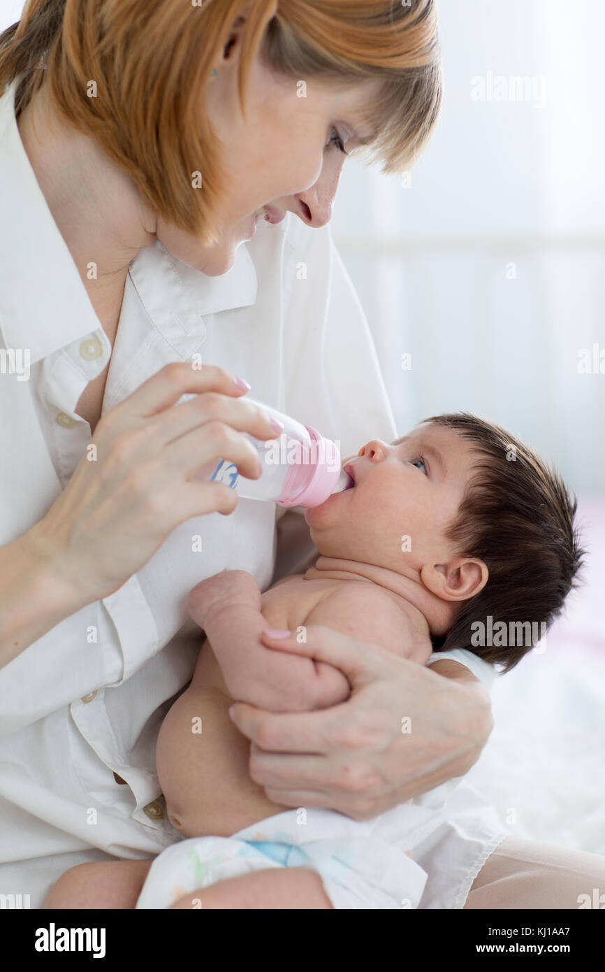 Madre dando baby acqua dalla bottiglia seduta sul letto Foto Stock