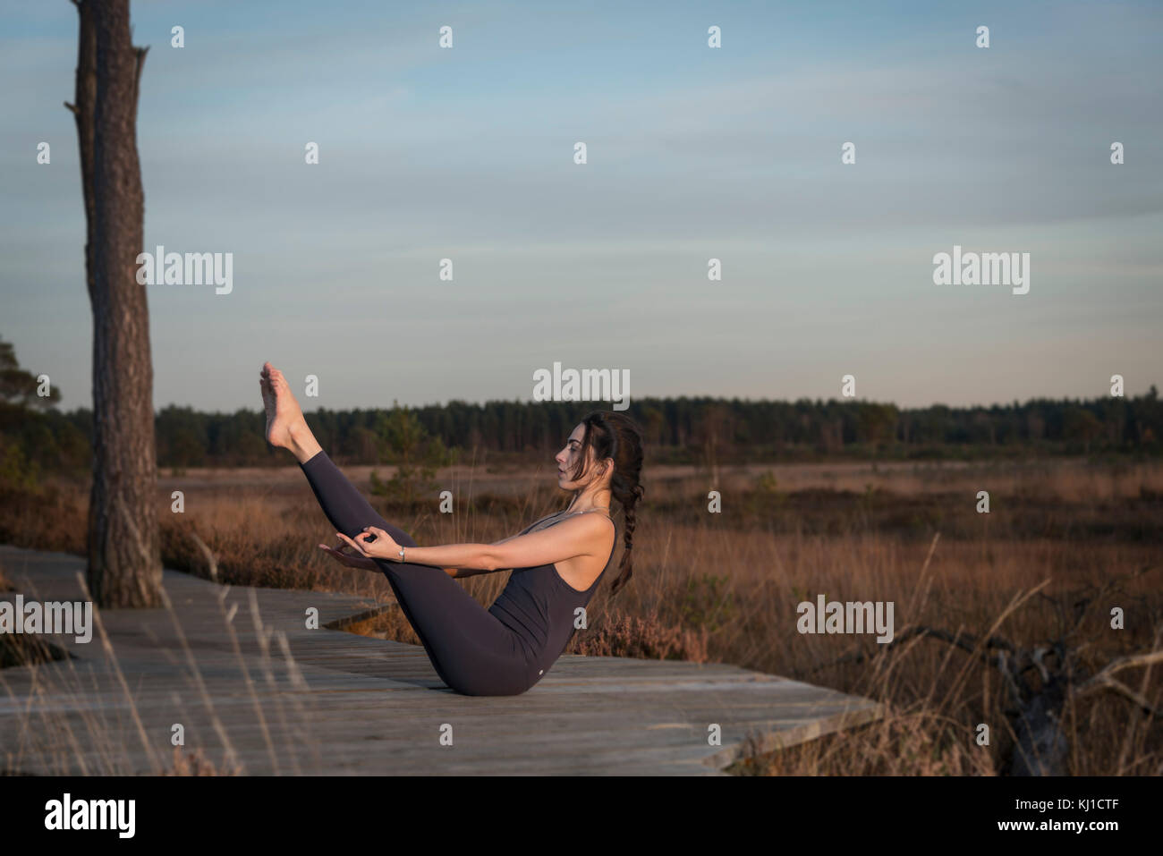 La donna a praticare yoga al di fuori in spazio aperto nella riserva naturale, facendo una barca posa. Foto Stock