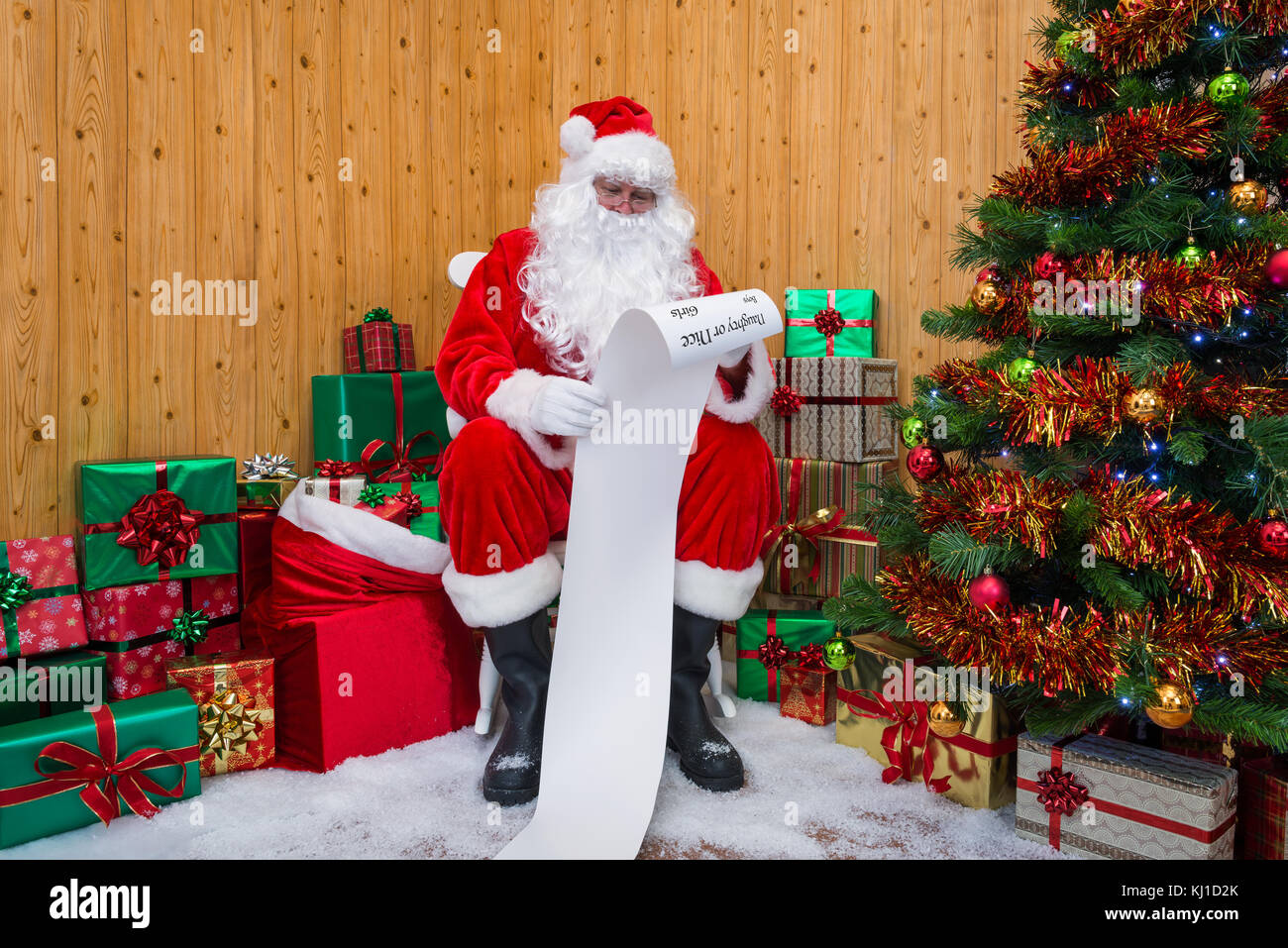 Babbo Natale nella sua grotta circondata da un albero di Natale con regali e regalo caselle controllo della naughty o Nizza elenco Foto Stock
