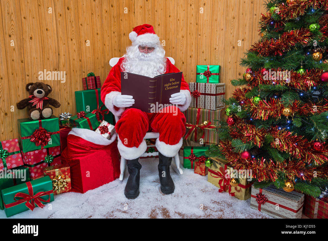 Babbo Natale seduto nella sua grotta circondata da una struttura ad albero con presenta e dono scatole avvolto mentre legge il suo libro preferito - la notte prima di chri Foto Stock