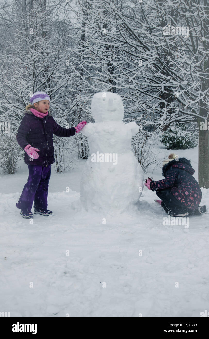 Dei bambini felici ennjoying atmosfera invernale in parcheggio coperto da neve giocando e costruire un pupazzo di neve Foto Stock
