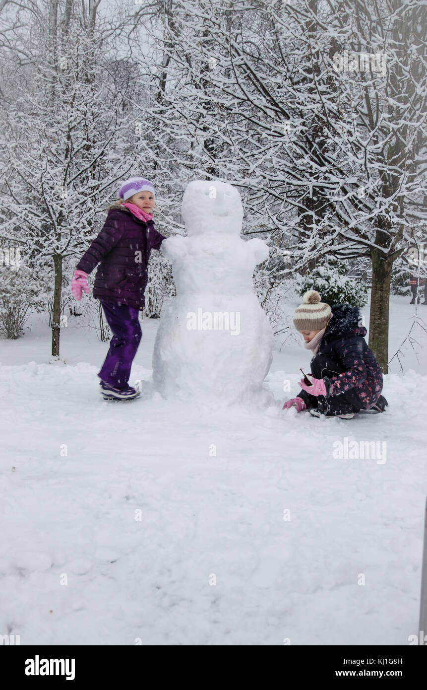 Due bambini felici le ragazze sorelle costruire un pupazzo di neve in inverno freddo park Foto Stock