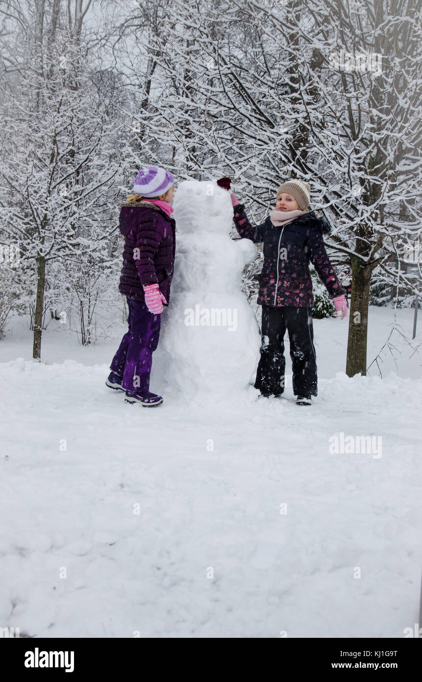 Dei bambini felici godendo di atmosfera invernale in parcheggio coperto da neve giocando e costruire un pupazzo di neve Foto Stock