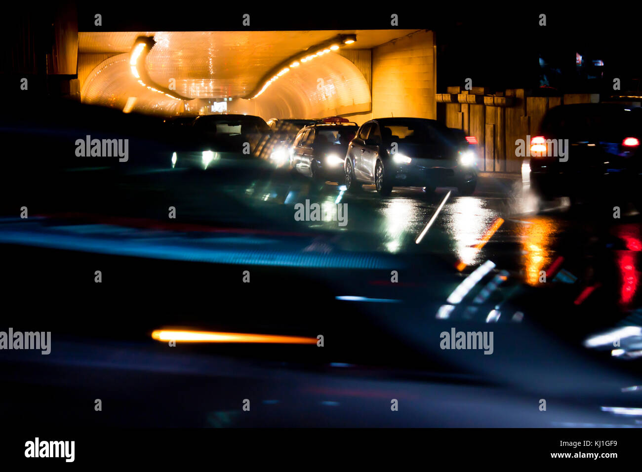 Il traffico di notte di pioggia per le strade delle città. vetture accodate all'uscita del tunnel in attesa presso l'intersezione durante la guida di veicoli in movimento passato, vista frontale con display da Foto Stock