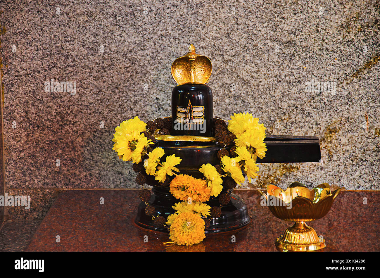 Shivling nero con fiore giallo garland . Un tradizionale lit Diya o piccola lampada in ottone. Patit Pavan Sri Ram Mandir, Belgavi, Karnataka, India Foto Stock