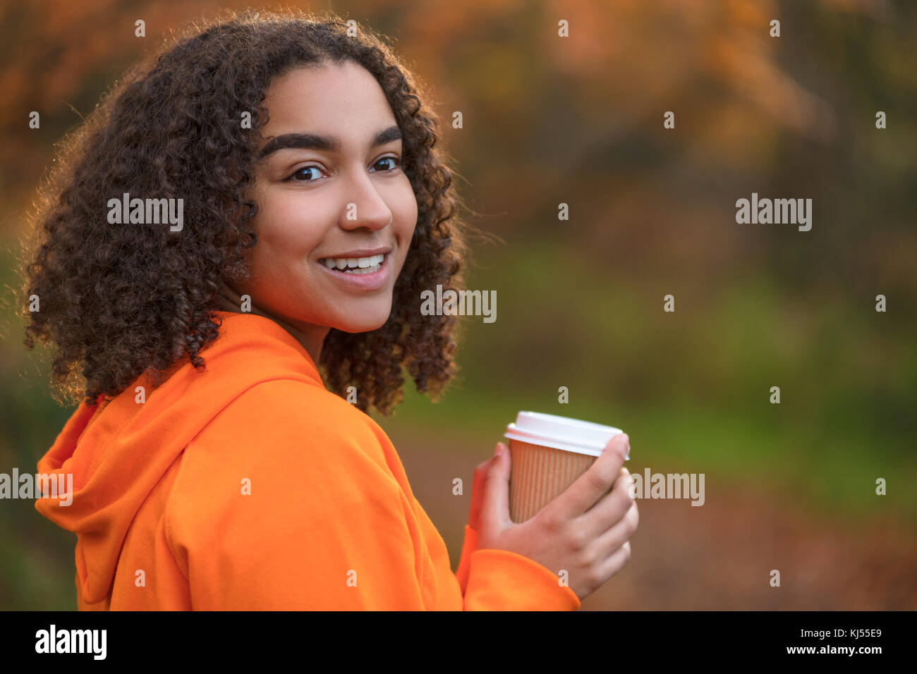 Bella felice razza mista americano africano ragazza adolescente femmine giovane donna sorridente con perfetta denti bianchi,di bere il caffè o il tè all'aperto in autunno Foto Stock