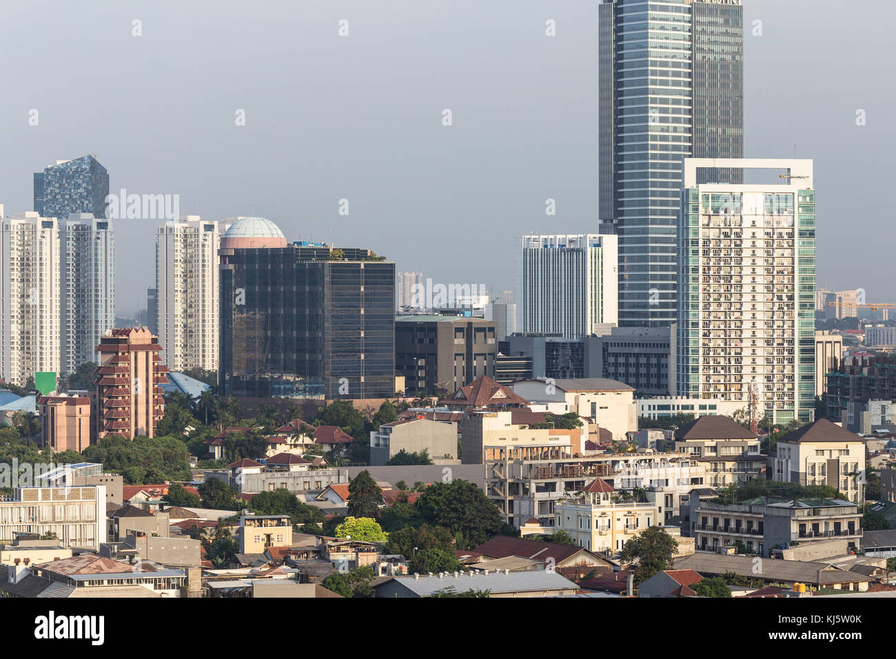 Vista aerea di un basso edificio residenziale in contrasto con un moderno condominio e torri di uffici nel cuore di Jakarta, Indonesia città capitale. Foto Stock