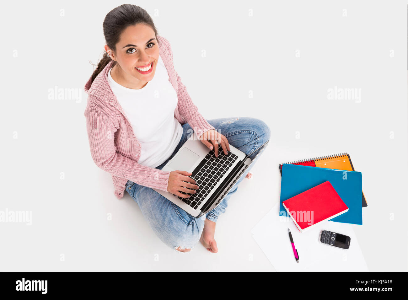 Giovane studentessa seduta con le gambe incrociate a lavorare con un computer portatile, isolato su sfondo bianco Foto Stock