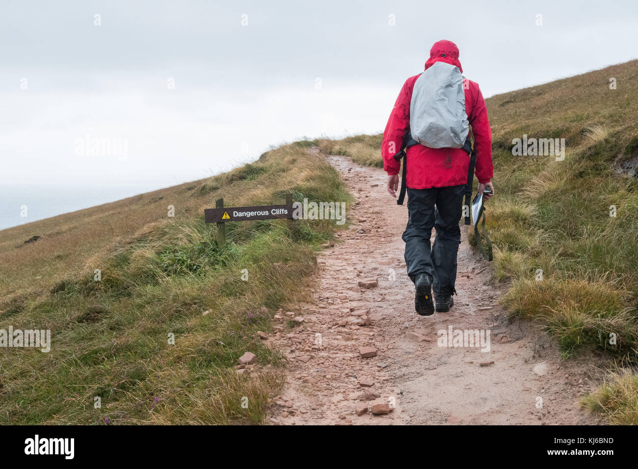 Uomo che cammina sul sentiero Old Man of Hoy in vento e pioggia passando pericoloso falesie segno, Hoy, Orkney, Scozia, Regno Unito Foto Stock