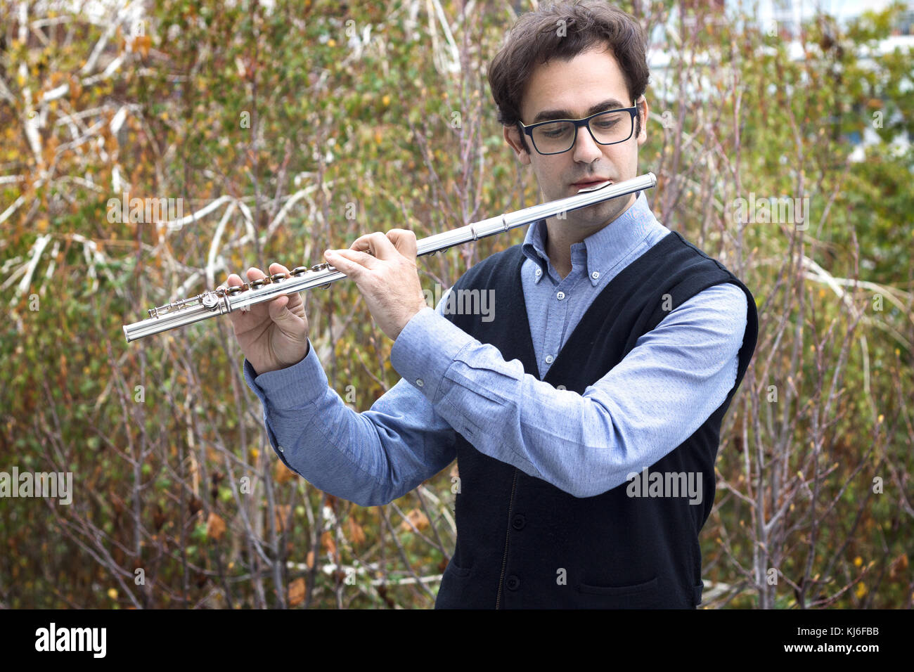 Un maschio flautista giocando a Silver flauto traverso all'aperto, indossare occhiali. Foto Stock