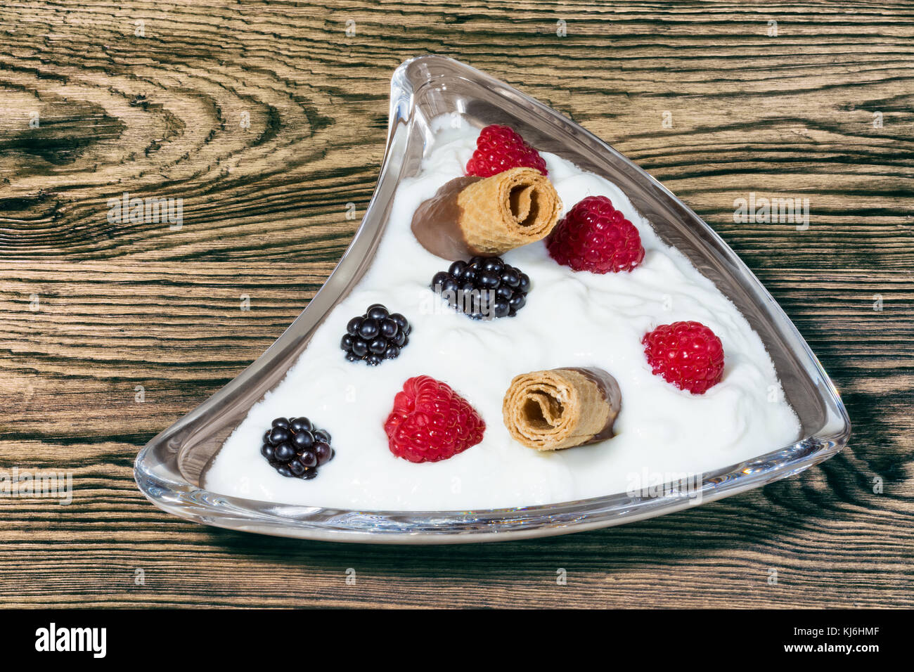 Dolce tentazione con frutta fresca e biscotti. ciotola di vetro con yogurt, lamponi e more su sfondo di legno. Foto Stock