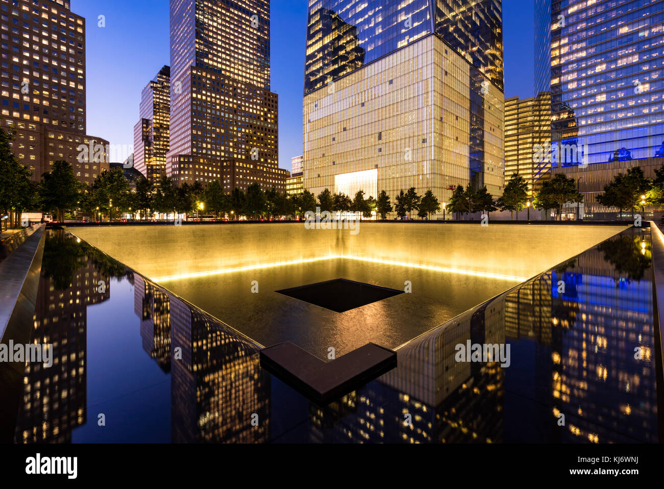 Il Nord Pool riflettente illuminato al crepuscolo con vista di One World Trade Center. La parte inferiore di Manhattan, 9/11 Memorial & Museum di New York City Foto Stock