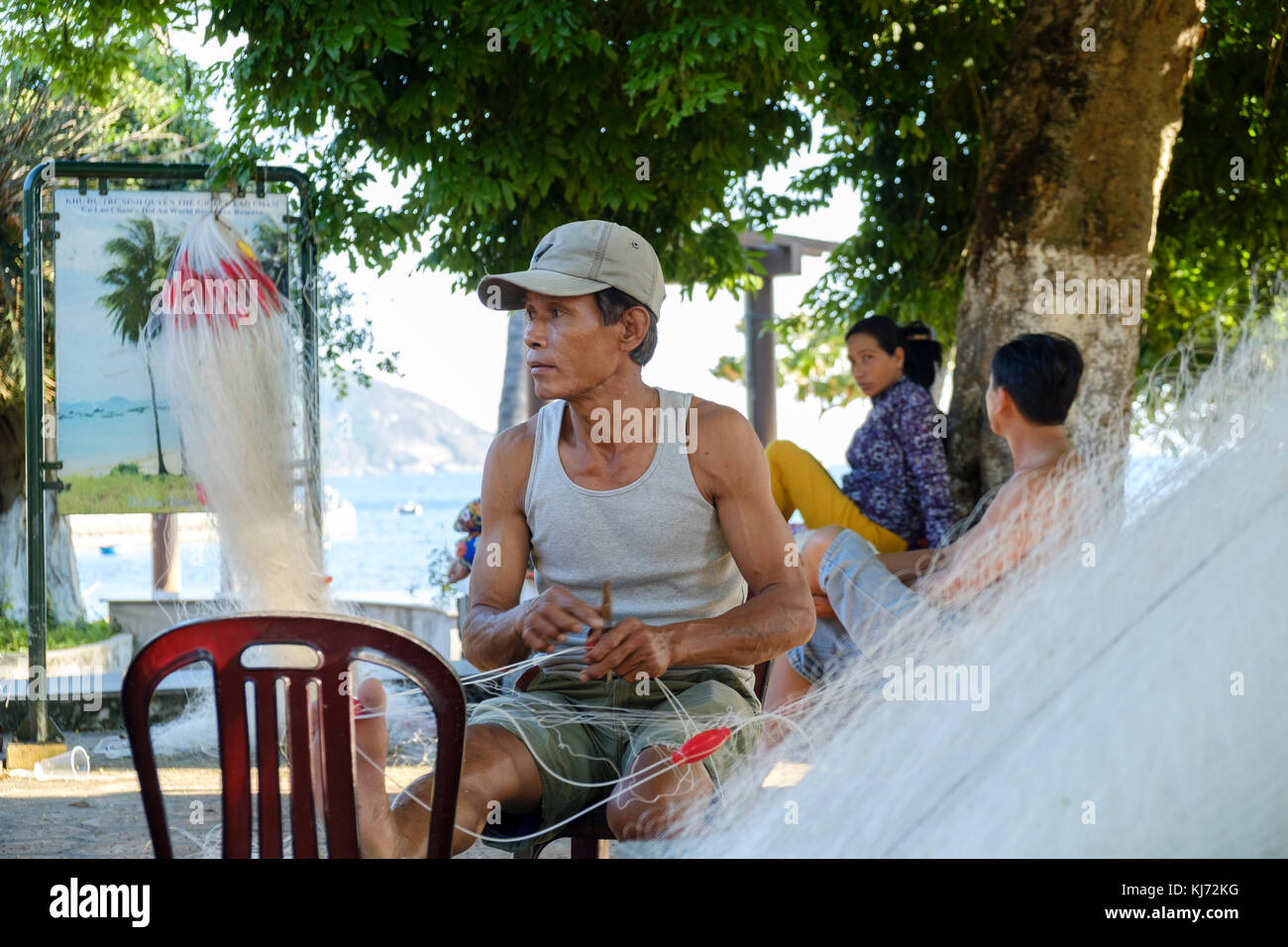 Pescatore vietnamita riparando la sua rete da pesca in un villaggio costiero Foto Stock