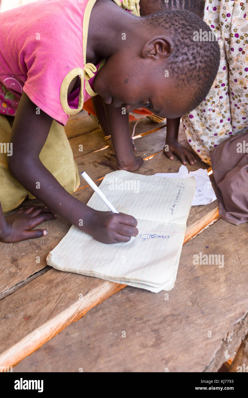 Giovane ragazza ugandese di scrittura e disegno in un esercizio libro all'ombra di un mercato non utilizzati in stallo, Uganda, Africa Foto Stock