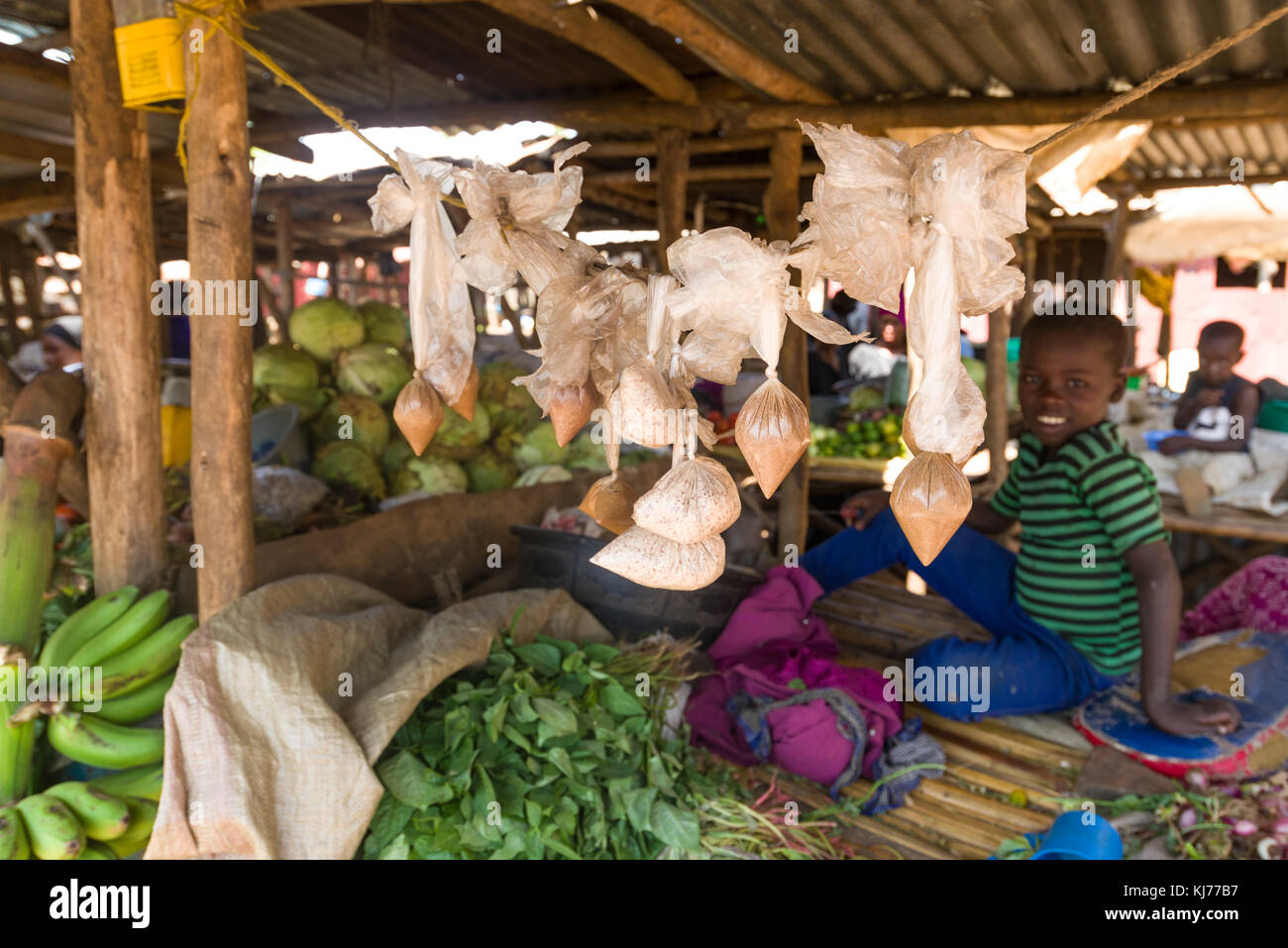 Sacchetti di arrow-polvere sul display alla frutta e verdura in stallo un mercato con ragazzo sullo sfondo l'ombra, Uganda, Africa Foto Stock