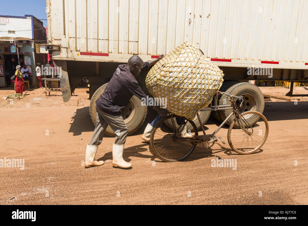 .Due uomini ugandesi a piedi con un sacco di grandi dimensioni su una bicicletta su una strada polverosa, Uganda, Africa orientale Foto Stock