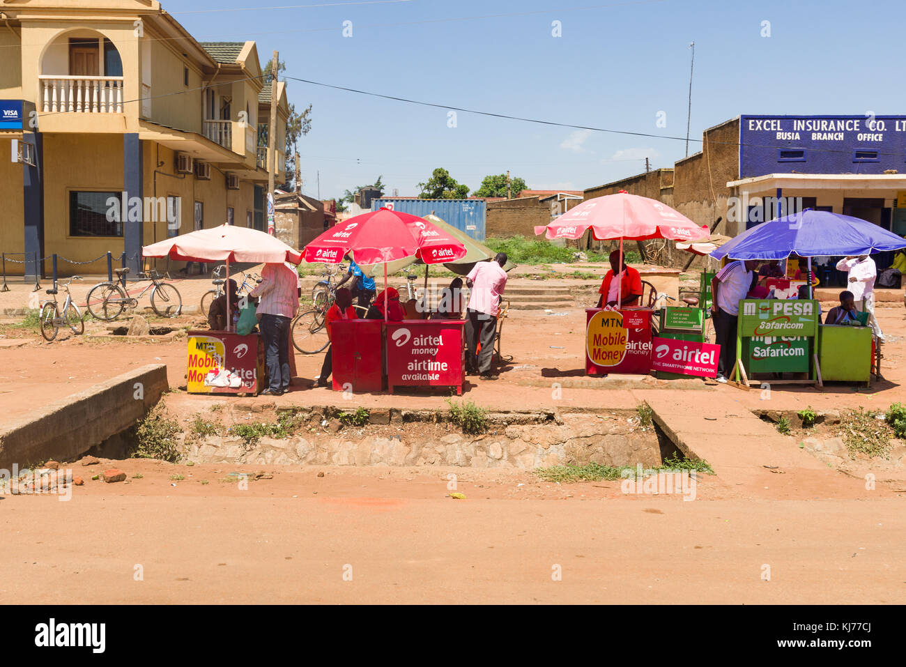 .Una fila di platea con ombrelloni e gente che vende airtime per varie reti mobili per strada, Uganda, Africa orientale Foto Stock