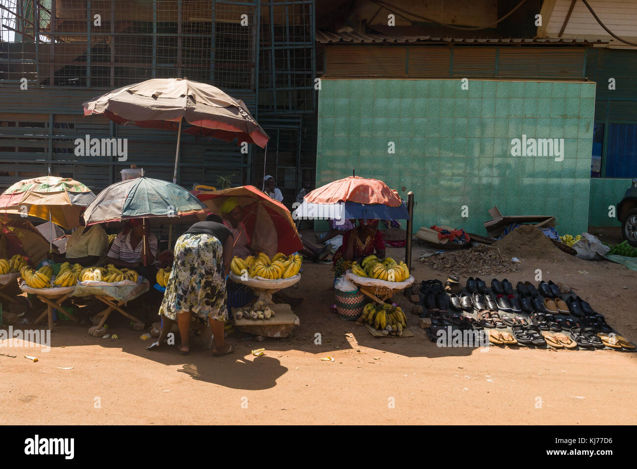 .Numerose piccole bancarelle di frutta e verdura con persone seduti all'ombra di ombrelloni dal lato della strada, Uganda, Africa Foto Stock