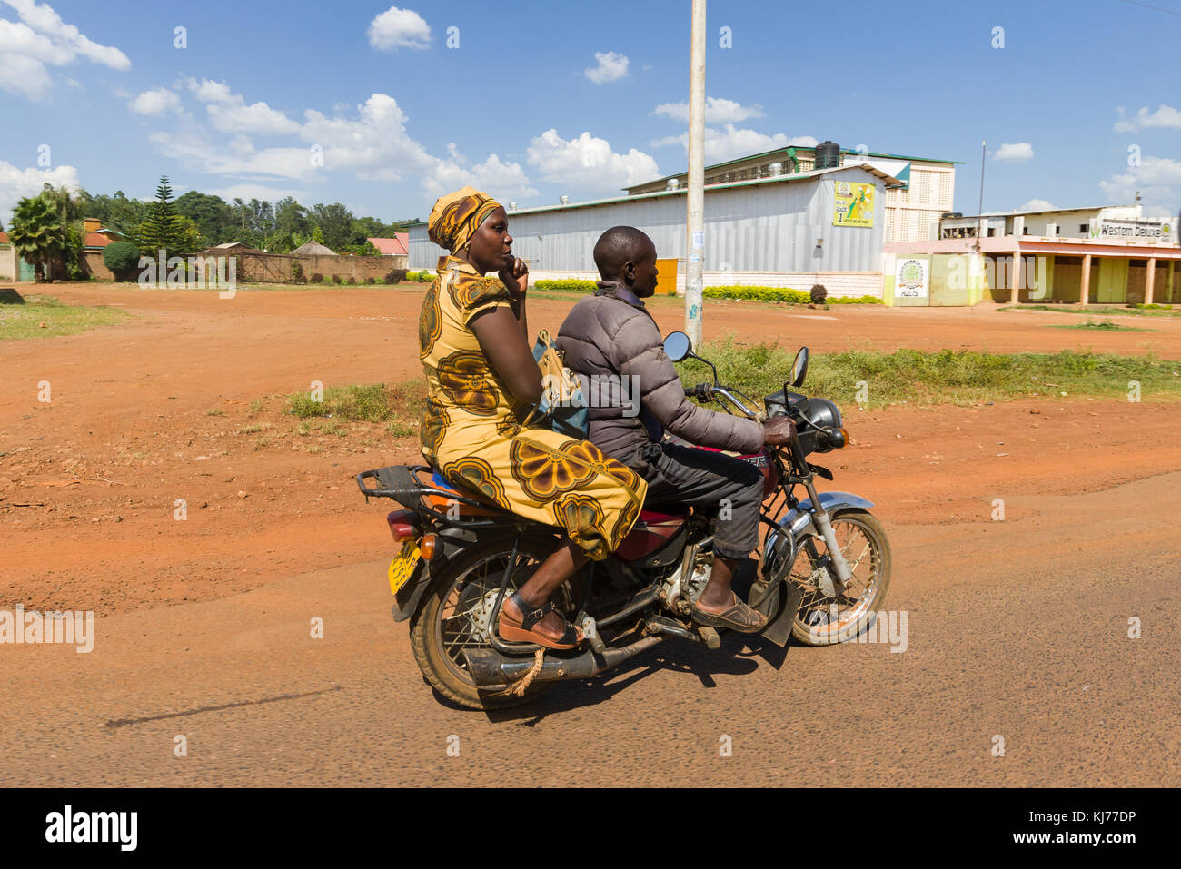 .Un ben vestito donna si siede sul retro di una boda boda motociclo taxi come esso comanda sulla strada, Uganda, Africa orientale Foto Stock