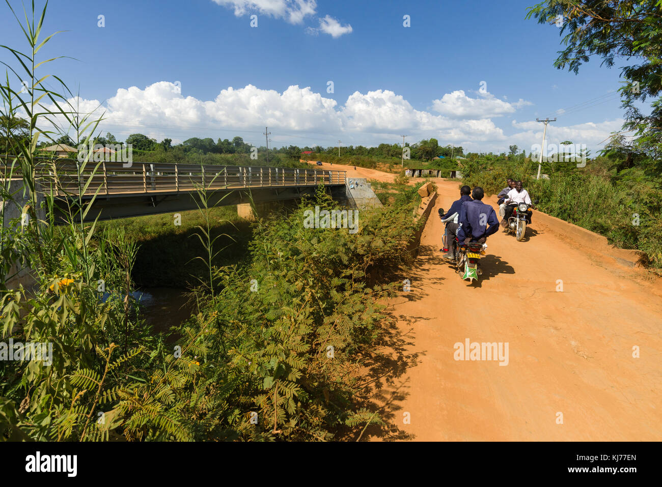 Moto boda boda taxi drive con passeggeri su una strada sterrata nei pressi di un ponte in costruzione, Kenya, Africa orientale Foto Stock