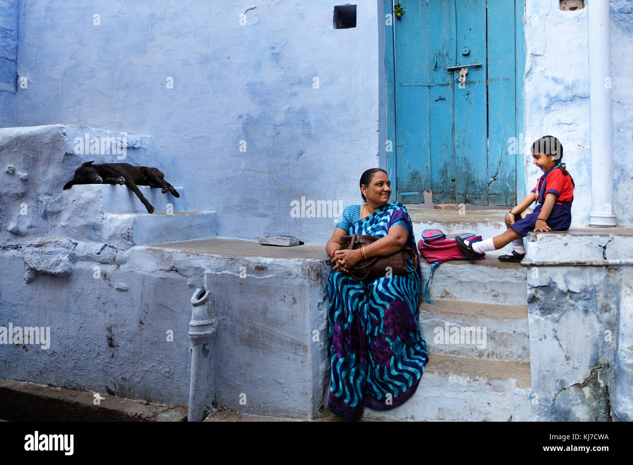 Happy little indian ragazza seduta sulle scale con la sua nonna a fronte di una casa blu in Jodhpur, Rajasthan, India. Foto Stock