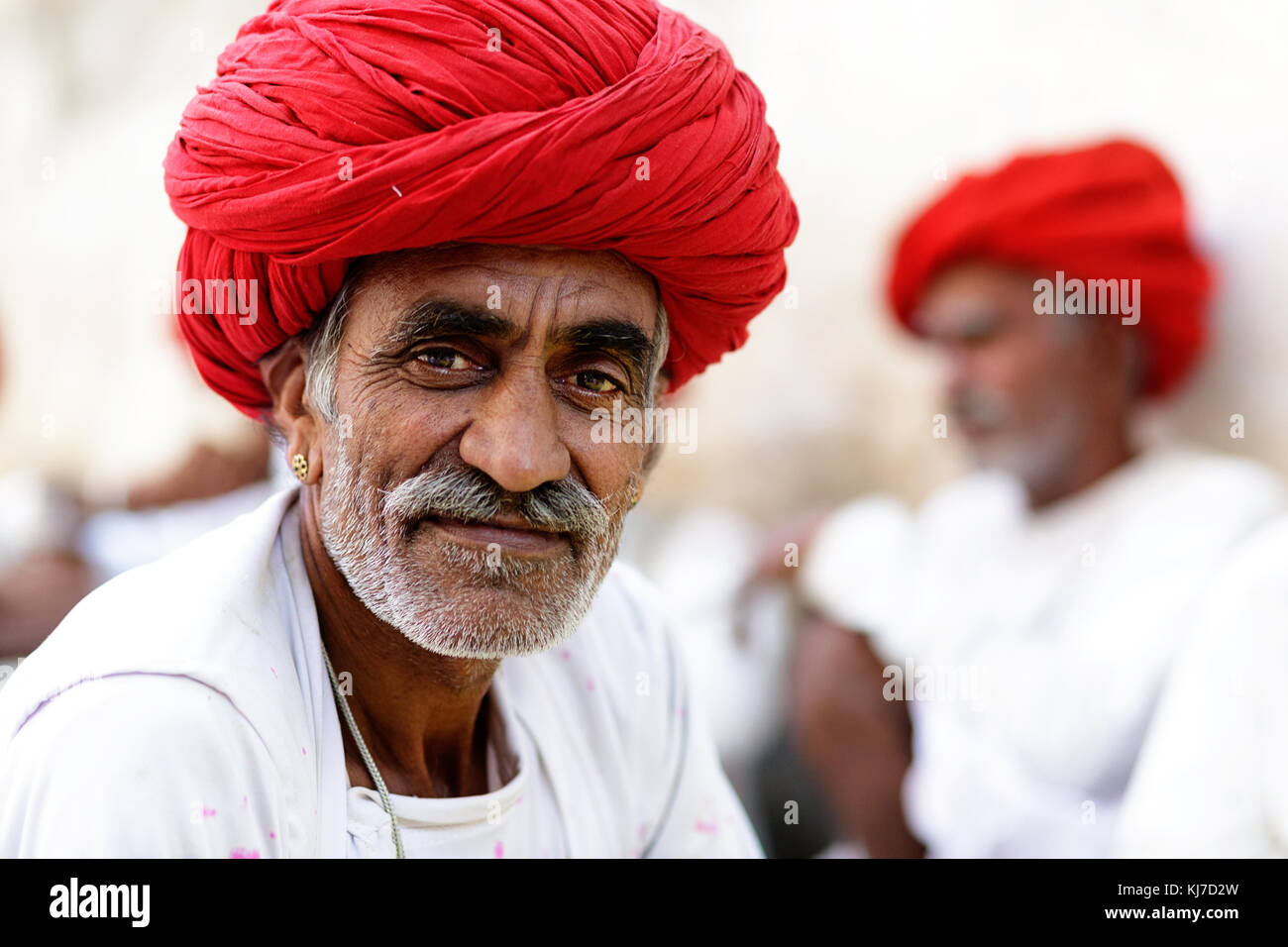 Ritratto di un anziano uomo dalla tribù Rabari con turbante rosso e i suoi amici nel retro, Rjasthan, India. Foto Stock