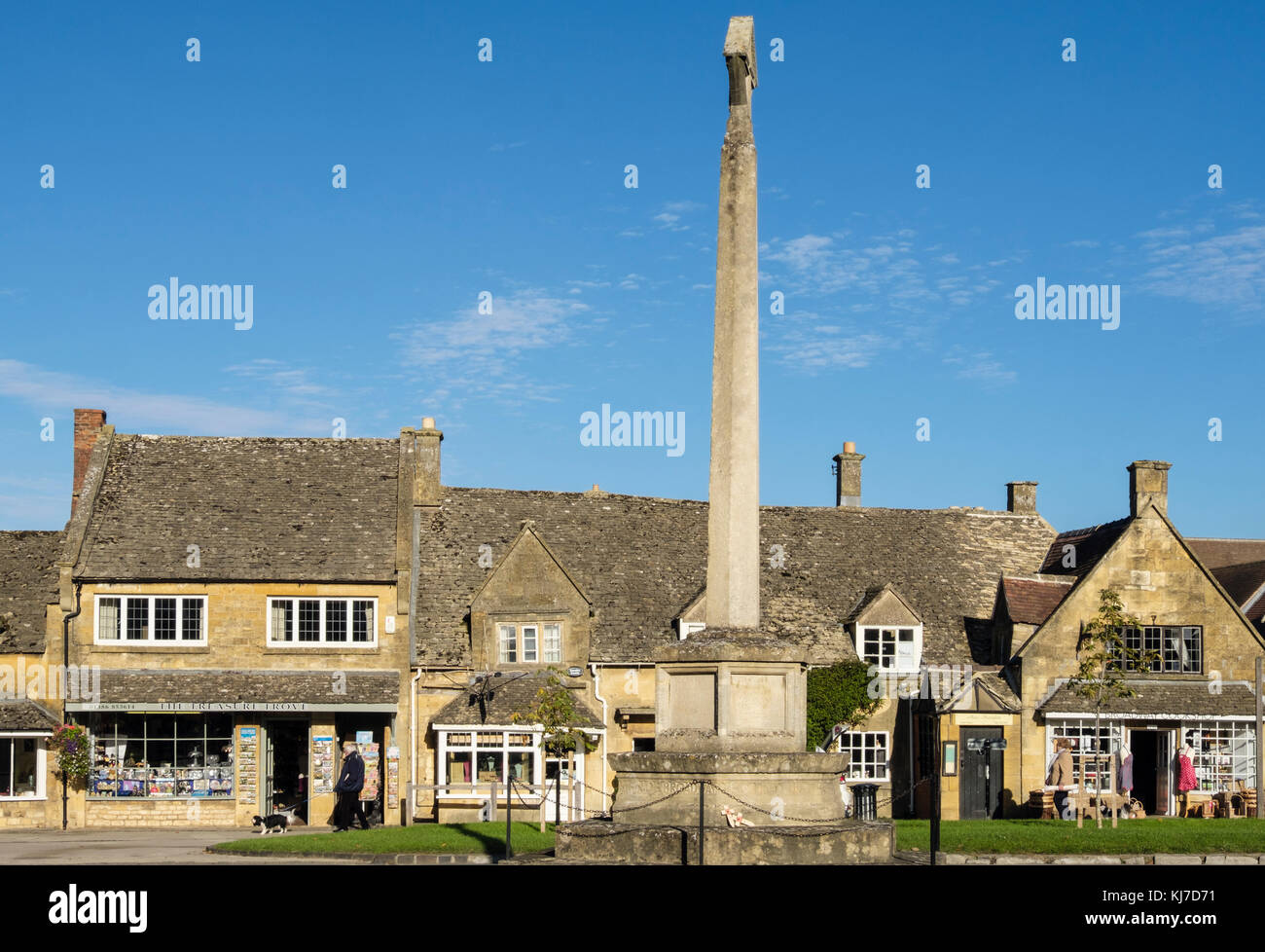 Memoriale di guerra croce di pietra in Cotswolds village center dominato da Cotswold stone negozi. High Street, Broadway, Worcestershire, Inghilterra, Regno Unito, Gran Bretagna Foto Stock