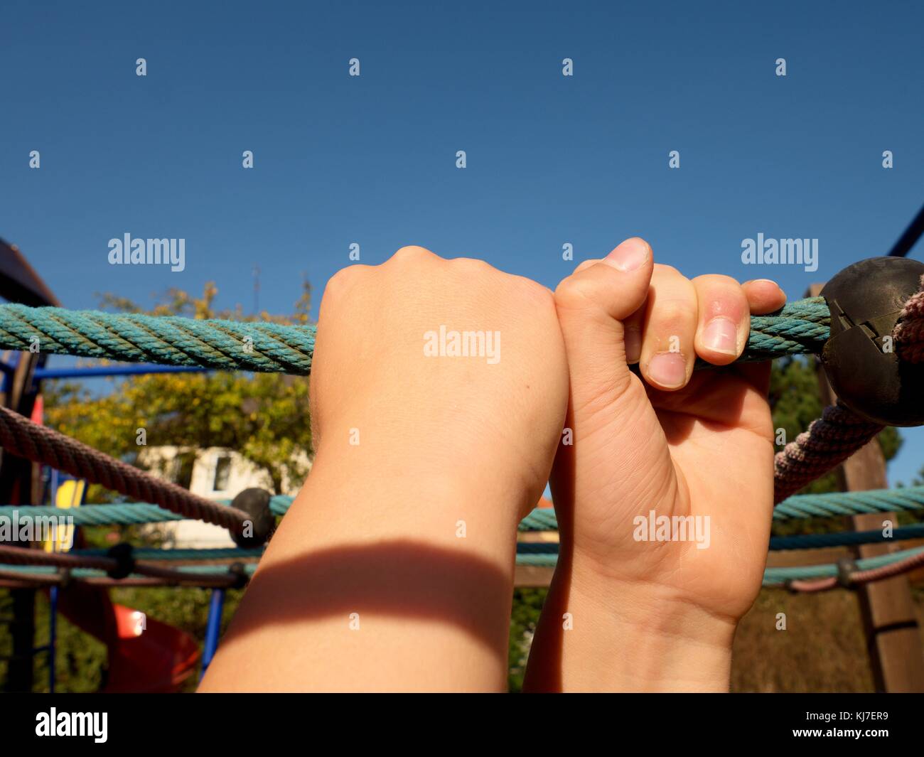 Ragazzo tenendo sulla corda blu bar in giardino per bambini parco giochi, cielo blu in background Foto Stock Ragazzo tenendo sulla corda blu bar in giardino per bambini parco giochi, cielo blu in background Foto Stock
