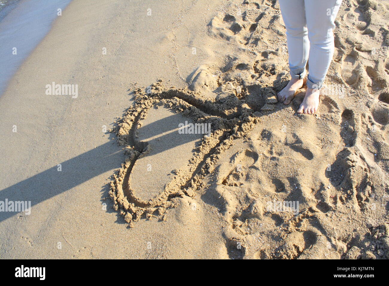 Una donna richiama un cuore nella sabbia sulla spiaggia per mostrare il concetto del suo amore sentimenti. Foto Stock