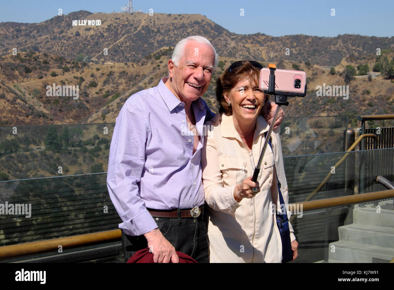 Coppia senior con selfie stick senior ridendo con la fotocamera del telefono cellulare e segno di Hollywood Griffith Park Observatory Los Angeles LA USA KATHY DEWITT Foto Stock
