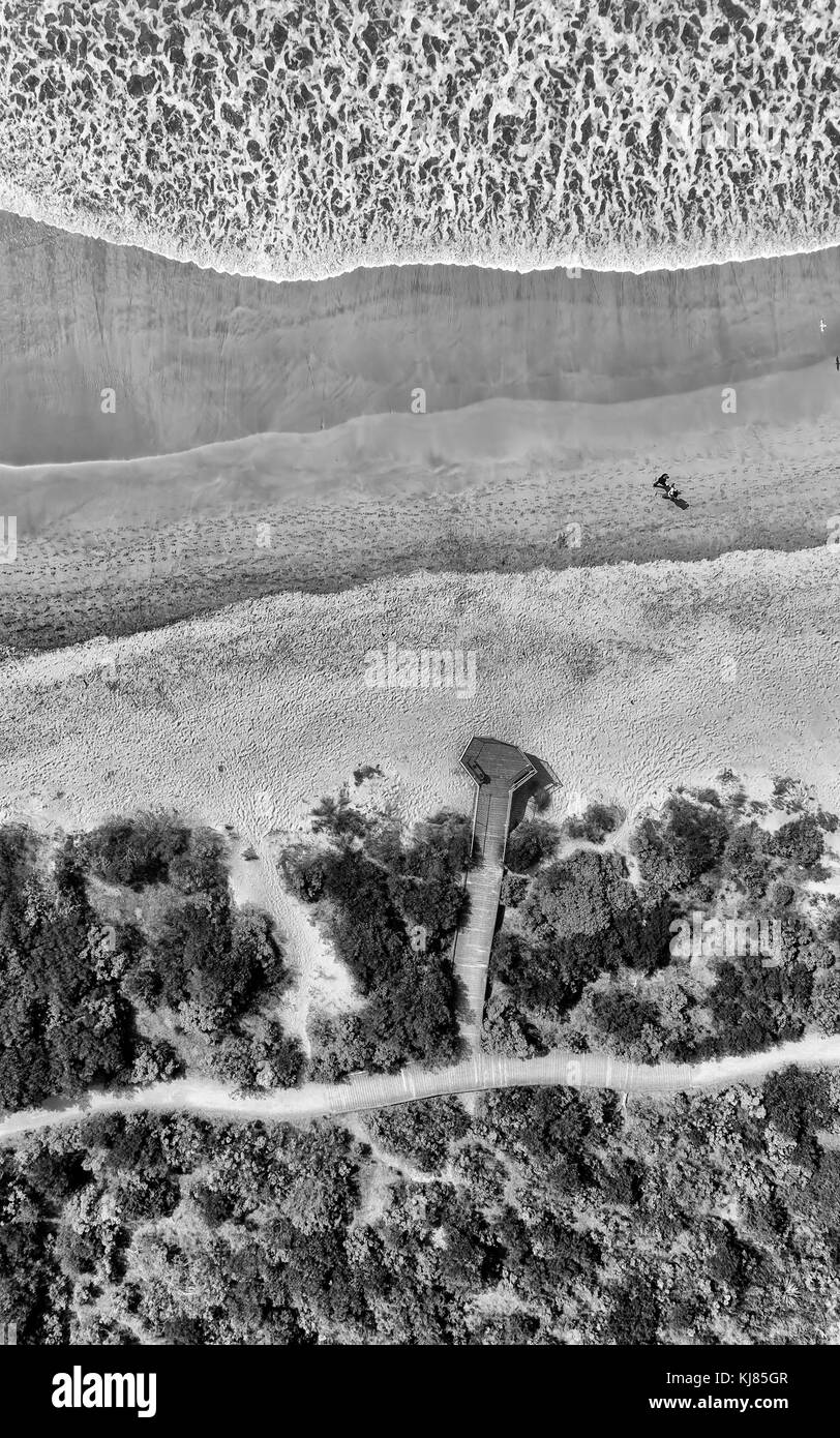 Antenna vista dall'alto in basso sul lungomare di tiding onde piane e spiaggia di sabbia con un paio di persone a piedi off vegetazione area parco in Apollo Bay town, au Foto Stock