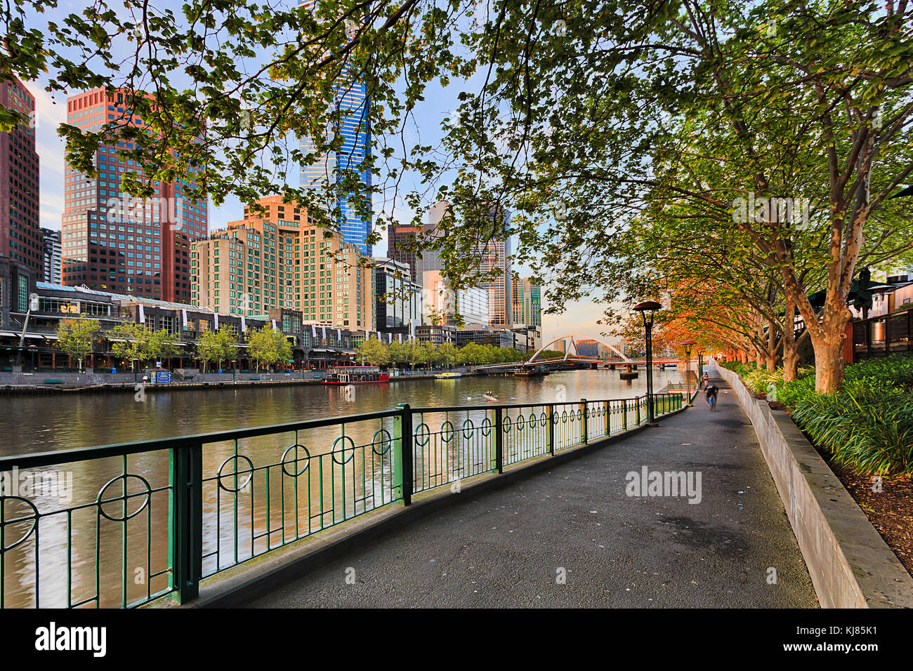 Il sentiero lungo il fiume Yarra nel centro cittadino di Melbourne sotto alberi frondosi rivolta southbank e walker ponte di mattina presto. Foto Stock