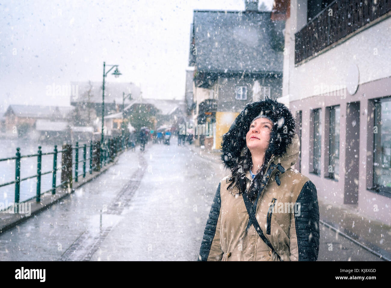 Felice periodo invernale con una bella ragazza godendo la nevicata, guardando il cielo, sulle strade di Hallstatt, uno dei siti del patrimonio mondiale in Foto Stock