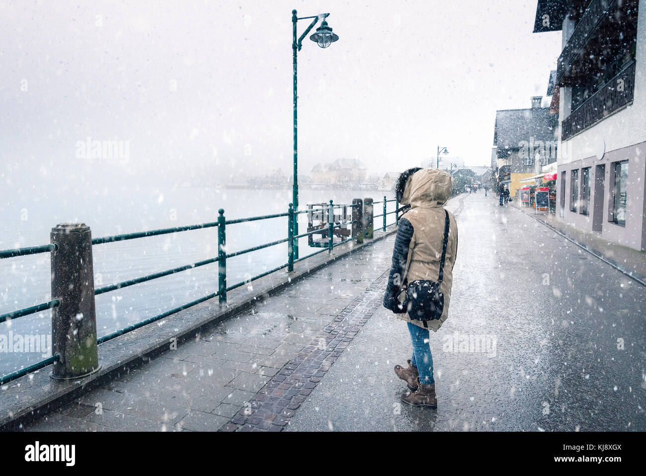 Inverno Meteo Tema immagine con una donna vestita di freddo, camminando sulla strada, sotto la nevicata, vicino al lago hallstatter, nella città di Hallstatt, aus Foto Stock