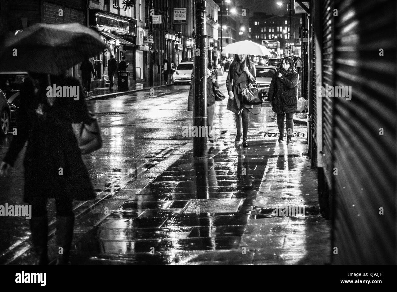 Sera vista guardando verso il basso Thomas Street, Manchester Central. Le donne sono illuminati da una finestra del negozio, come fanno il loro modo attraverso il lettore RUSH ore di pioggia Foto Stock
