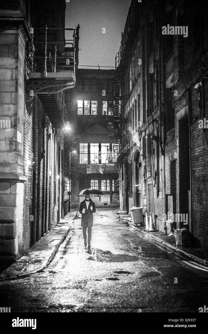 Vista la sera guardando giù mangle street da dale street, il centro di Manchester come un uomo fa il suo modo attraverso la pioggia con un ombrello. Foto Stock