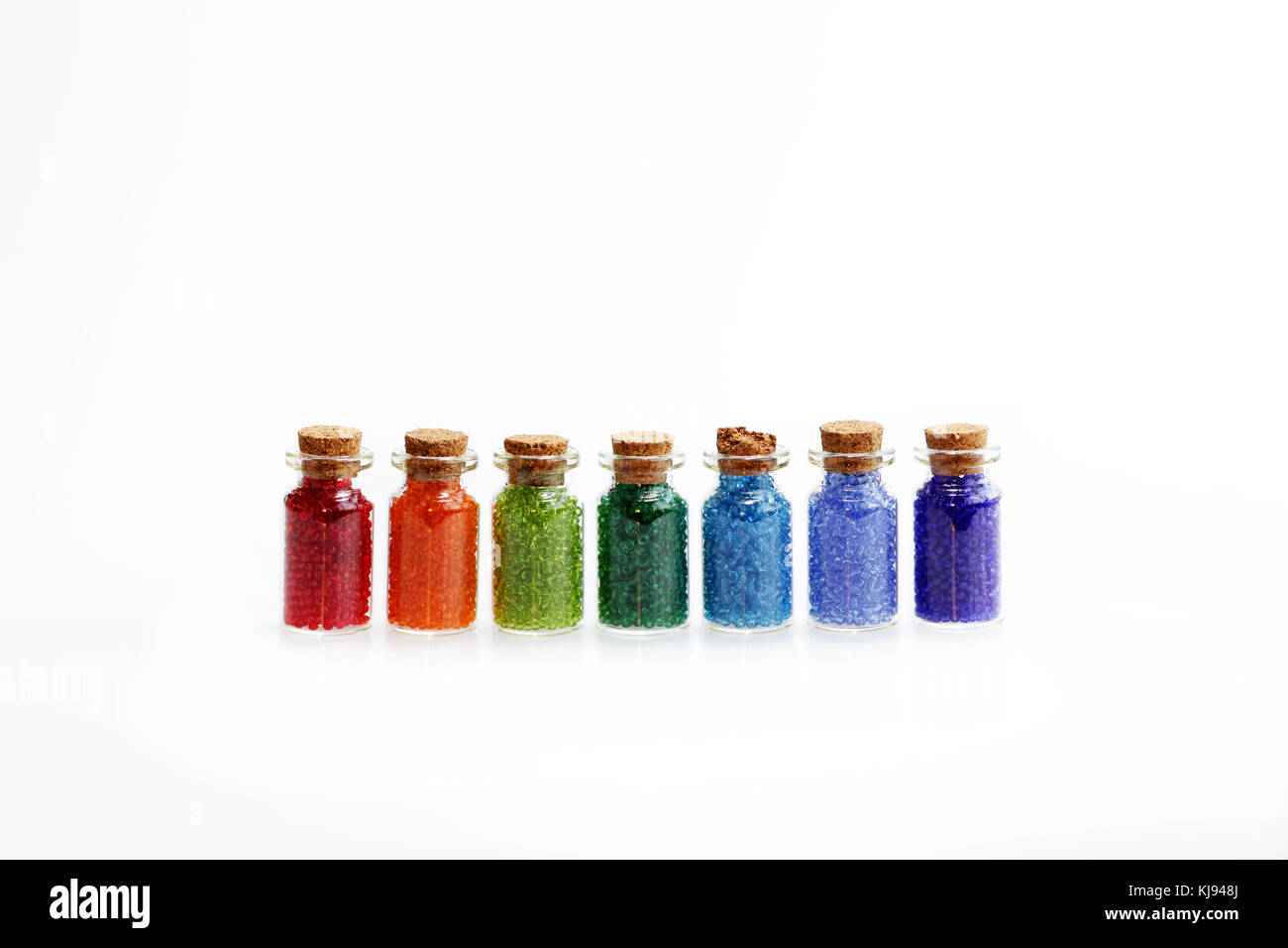 Sette piccoli bottiglie di vetro con un tappo di sughero, riempito con un  arcobaleno di colori di perle, su sfondo bianco Foto stock - Alamy