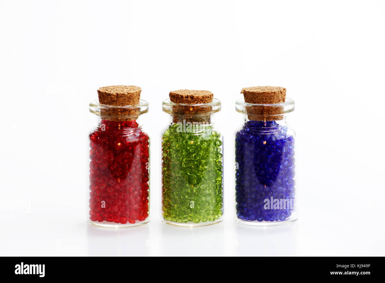 Tre piccole bottiglie di vetro con un tappo di sughero, riempito con un  arcobaleno di colori di perle, su uno sfondo bianco. rosso, verde e blu  Foto stock - Alamy