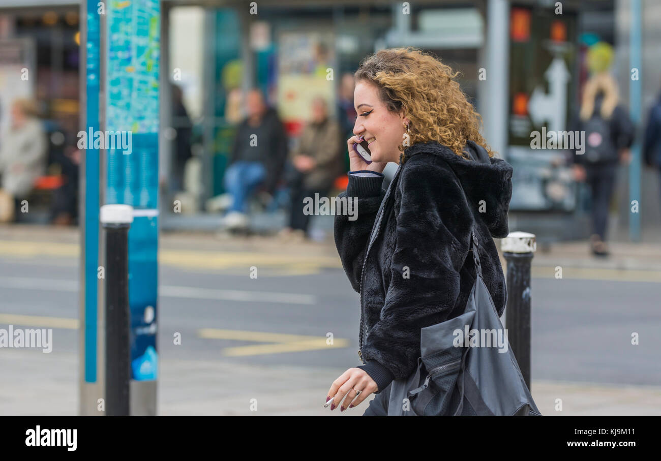 Giovane donna a camminare in una città mentre si parla di un telefono cellulare nel Regno Unito. Foto Stock