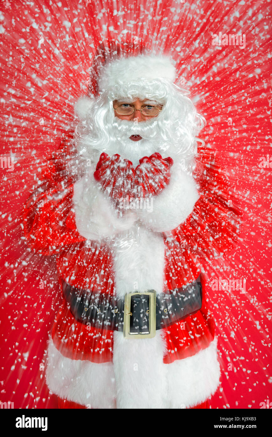 Santa Claus o babbo natale lavori di soffiaggio della neve verso di voi contro uno sfondo di colore rosso. Foto Stock
