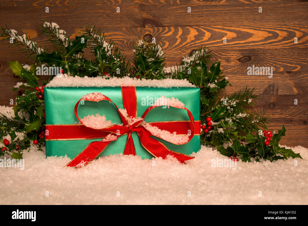 Regalo di natale regalo avvolto nella carta verde con nastro rosso con agrifoglio e neve contro uno sfondo di legno, copia dello spazio per il vostro messaggio. Foto Stock