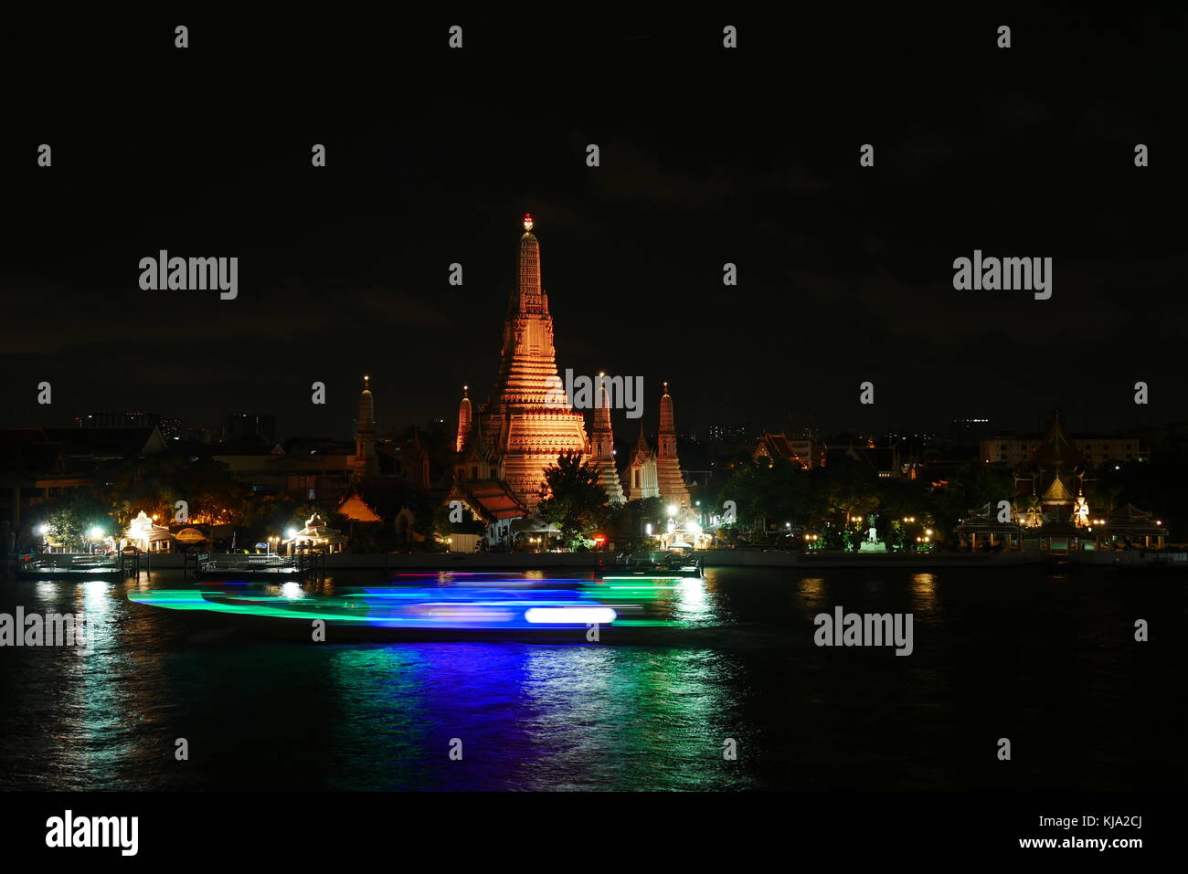 Una vista notturna di Wat Arun, il Tempio di Dawn a Bangkok, Thailandia, mentre una barca dalla lunga coda sta passando sul Fiume Chao Praya river. Foto Stock