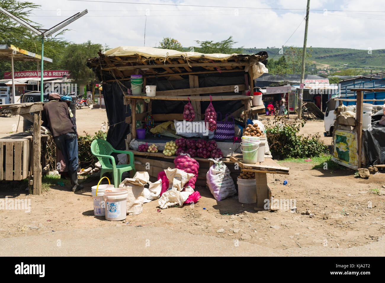 Un africano sorge dal suo stallo con frutta e verdura in vendita dal ciglio della strada, Kenya, Africa orientale Foto Stock