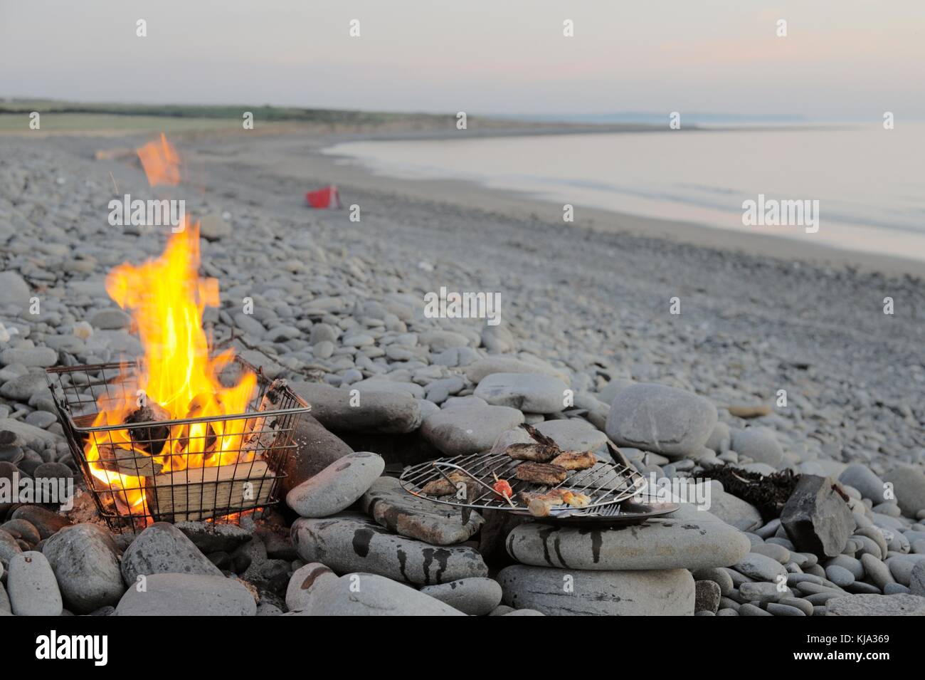 Resti di un pasto cucinato su un barbecue in un riutilizzato Shopping basket sulla spiaggia con tenda e defocussed persona in background Wales, Regno Unito Foto Stock